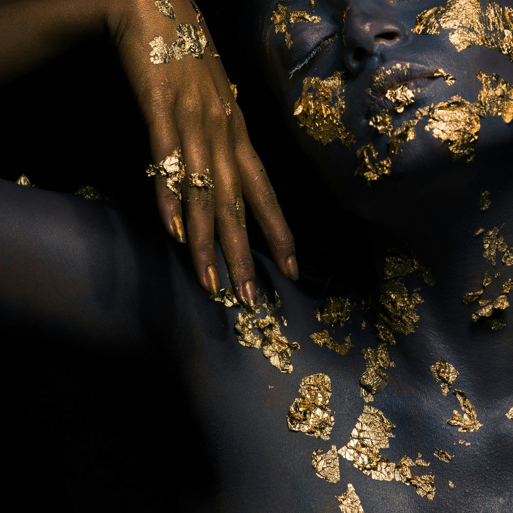 Person with gold leaf on their body against a dark background