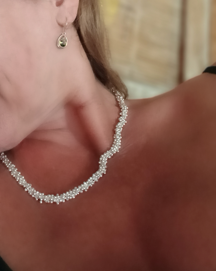 Close-up of a person wearing a silver hoop earring and a silver necklace with a blurred background