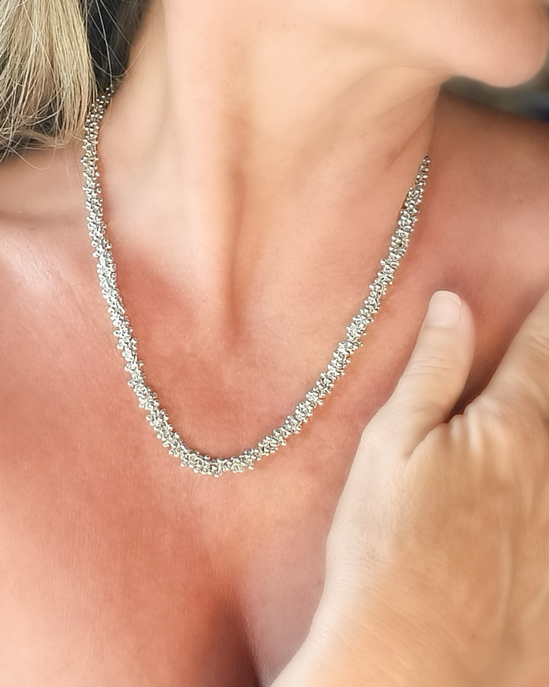 Close-up of a woman wearing a silver necklace and bracelet on a blurred background