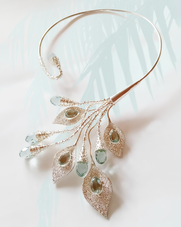 Delicate gold necklace with green gemstone pendants on a light background