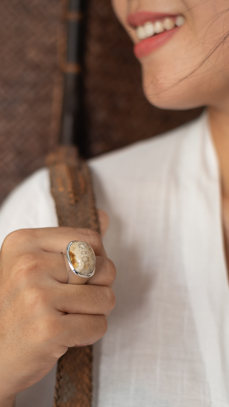 Woman wearing a white top with a close-up of her hand holding a brown leather strap, featuring a detailed ring.