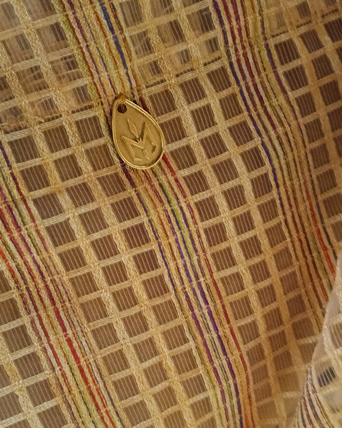 Close-up of a patterned fabric with a Natalie Noor logo engraved in nordic gold tag.