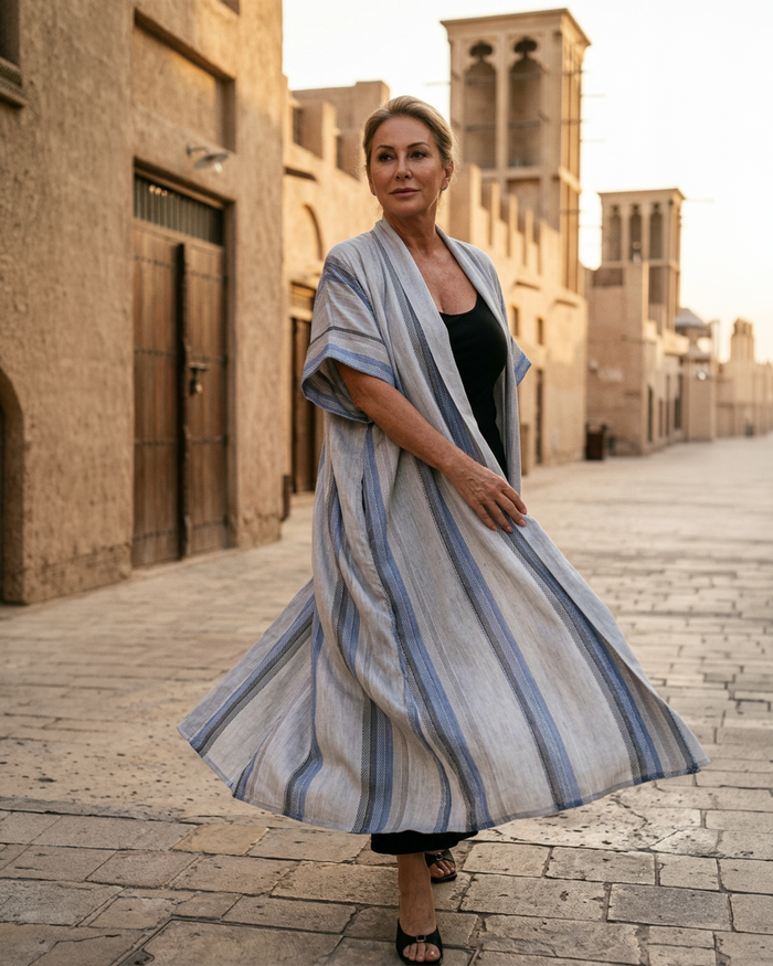 Natalie Noor wearing a long, striped robe in an traditional  middle-eastern street. From the Natalie Noor Sahara Resort Wear Collection.