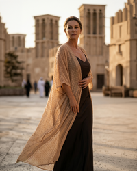 Natalie Noor in a long nude uragiri chiffon robe, over a black dress standing in front of the traditional architecture of Al Seef, Dubai.