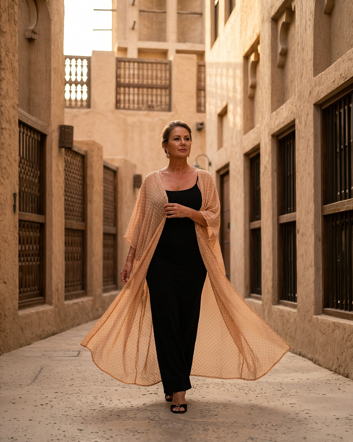 Natalie Noor in a black dress with a fluid nude uragiri chiffon robe, walking through an alleyway of old Dubai.
