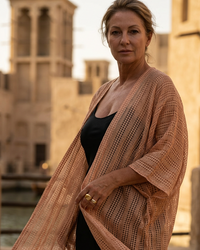 Natalie Noor wearing a long, light sun-kissed  jacquard robe over a black dress with a blurred architectural background. A Natalie Noor resort wear collection.