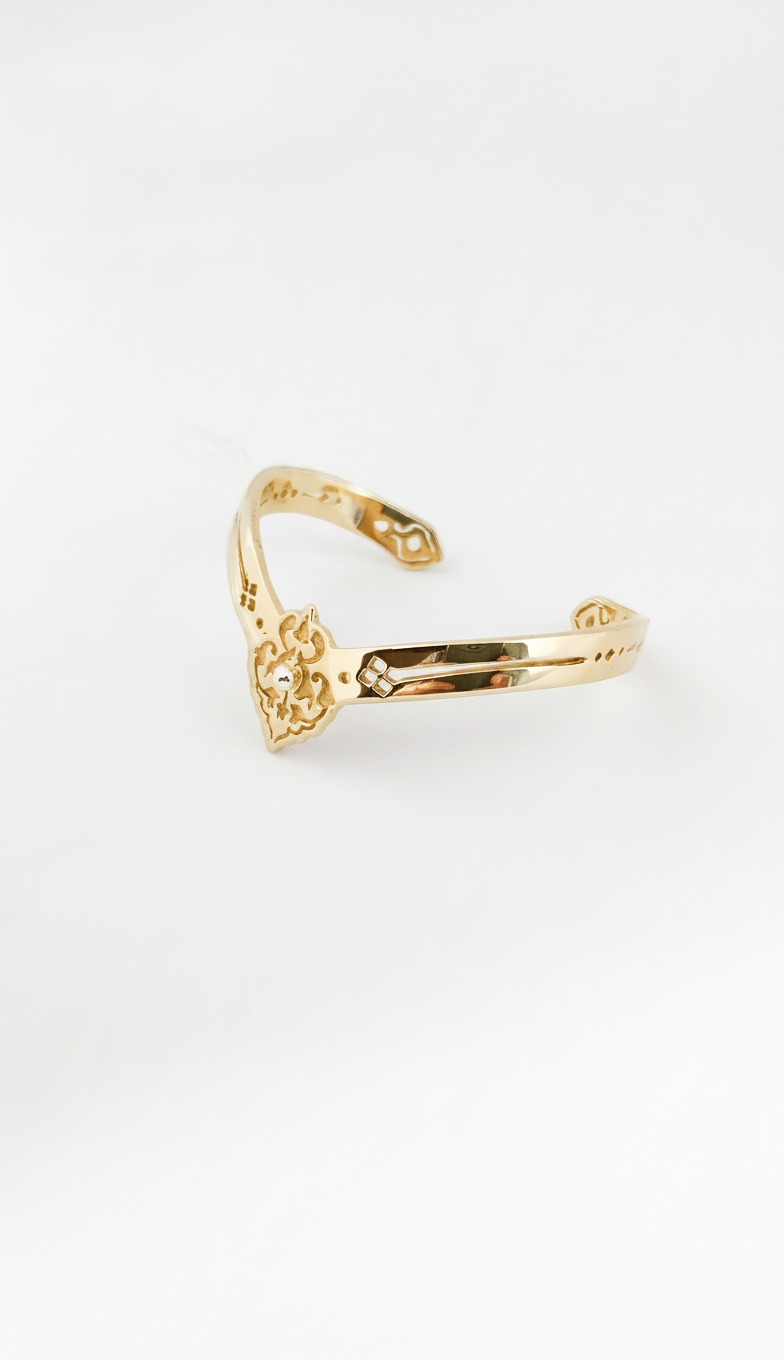 Golden cuff bracelet with a decorative design on a white background. Maison Natalie Noor, jewelry lit by Desire.
