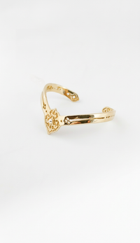 Golden cuff bracelet with a decorative design on a white background. Maison Natalie Noor, jewelry lit by Desire.
