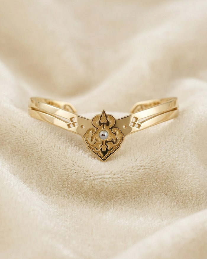 Golden cuff bracelet with a decorative clasp on a beige fabric background.