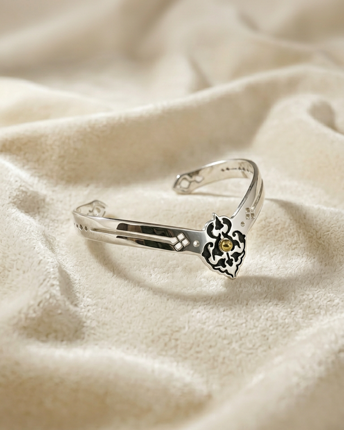 Silver bracelet with a heart-shaped clasp on a beige fabric background. Sharafeh Collection by Natalie Noor - Jewelry lit by Desire