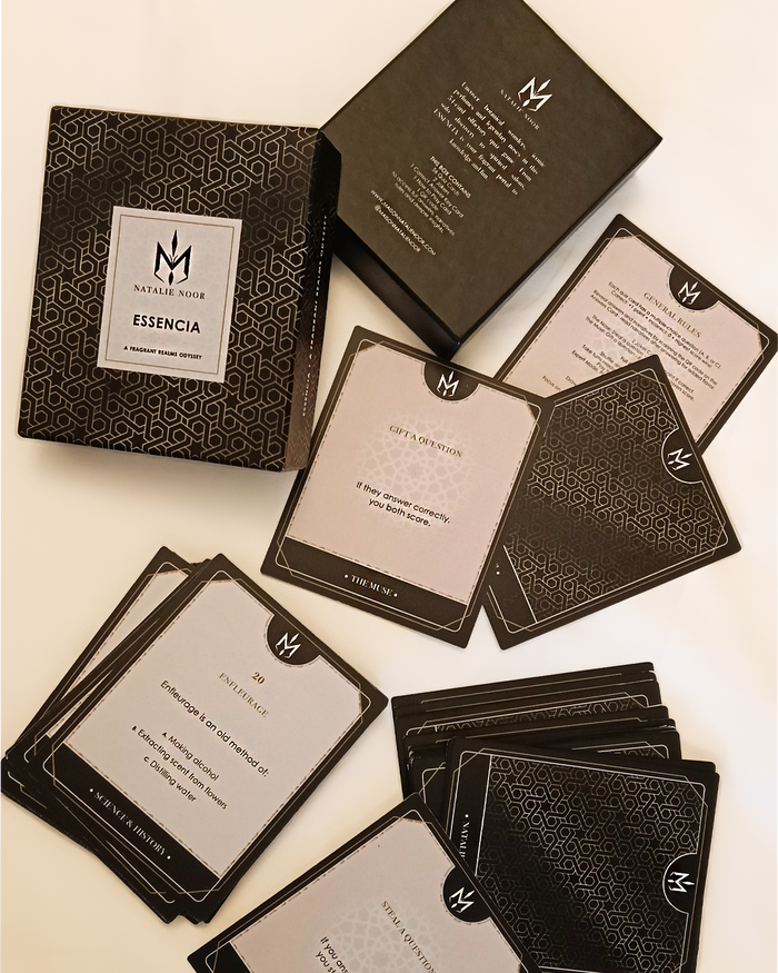 Black and gold packaging with cards featuring a logo on a beige background. Maison Natalie Noor, intelligence is sexy.