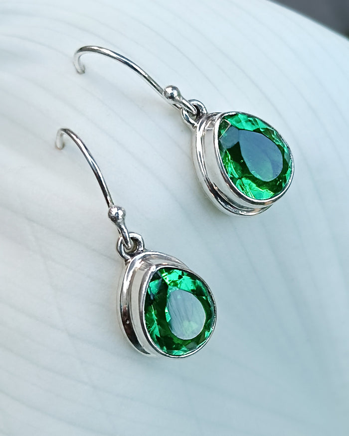 Silver earrings with green obsidian gemstones on a white background. Maison Natalie Noor, jewelry lit by desire.