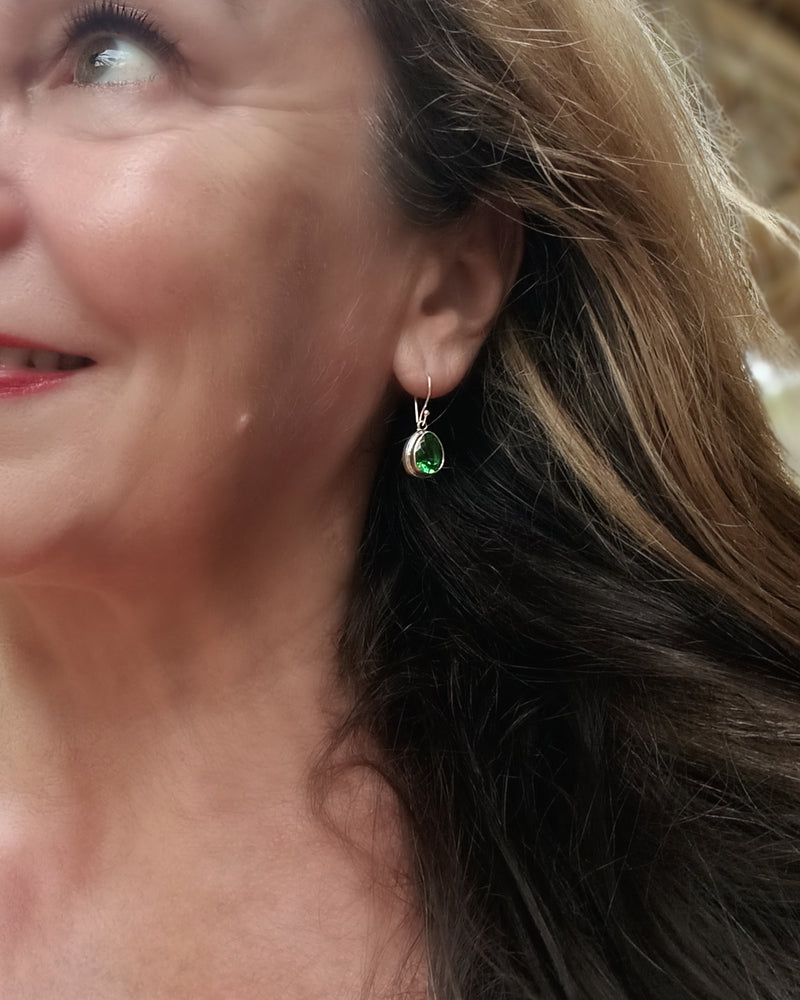 Close-up of a woman wearing a green obsidian drop earring. Maison Natalie Noor, jewelry lit by desire.