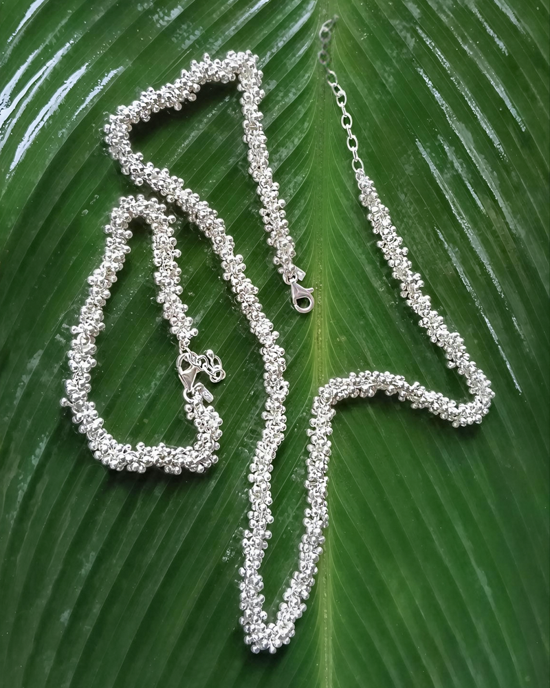 Silver necklace and bracelet on a green leaf. Natalie Noor, jewelry lit by desire