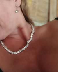 Close-up of a person wearing a silver hoop earring and a silver necklace with a blurred background. Natalie Noor, jewelry lit by desire.