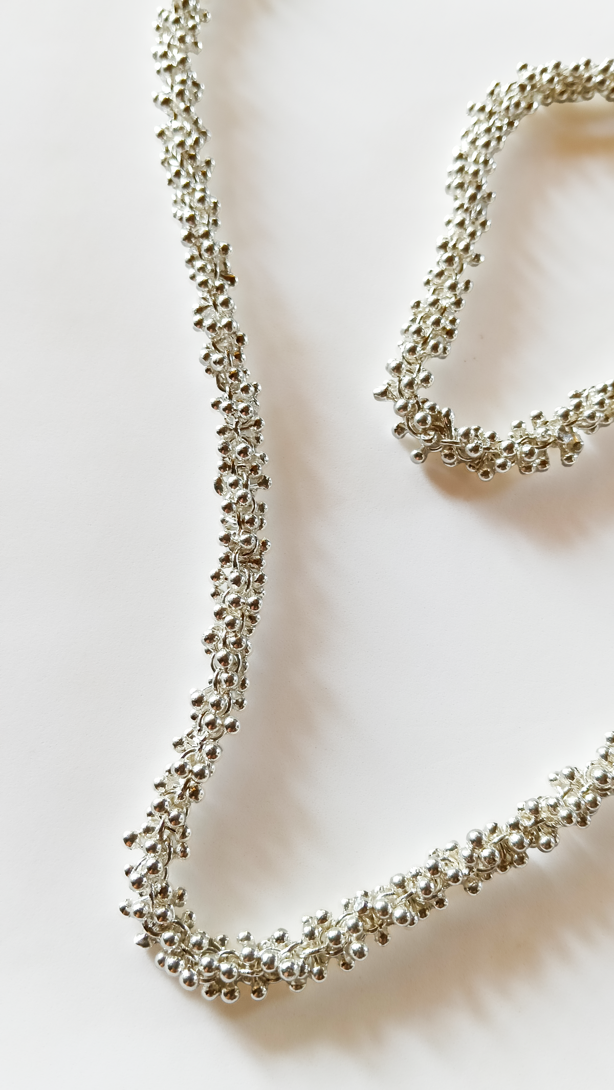 Silver necklace and bracelet set on a soft beige background. Maison Natalie Noor, jewelry lit by desire.