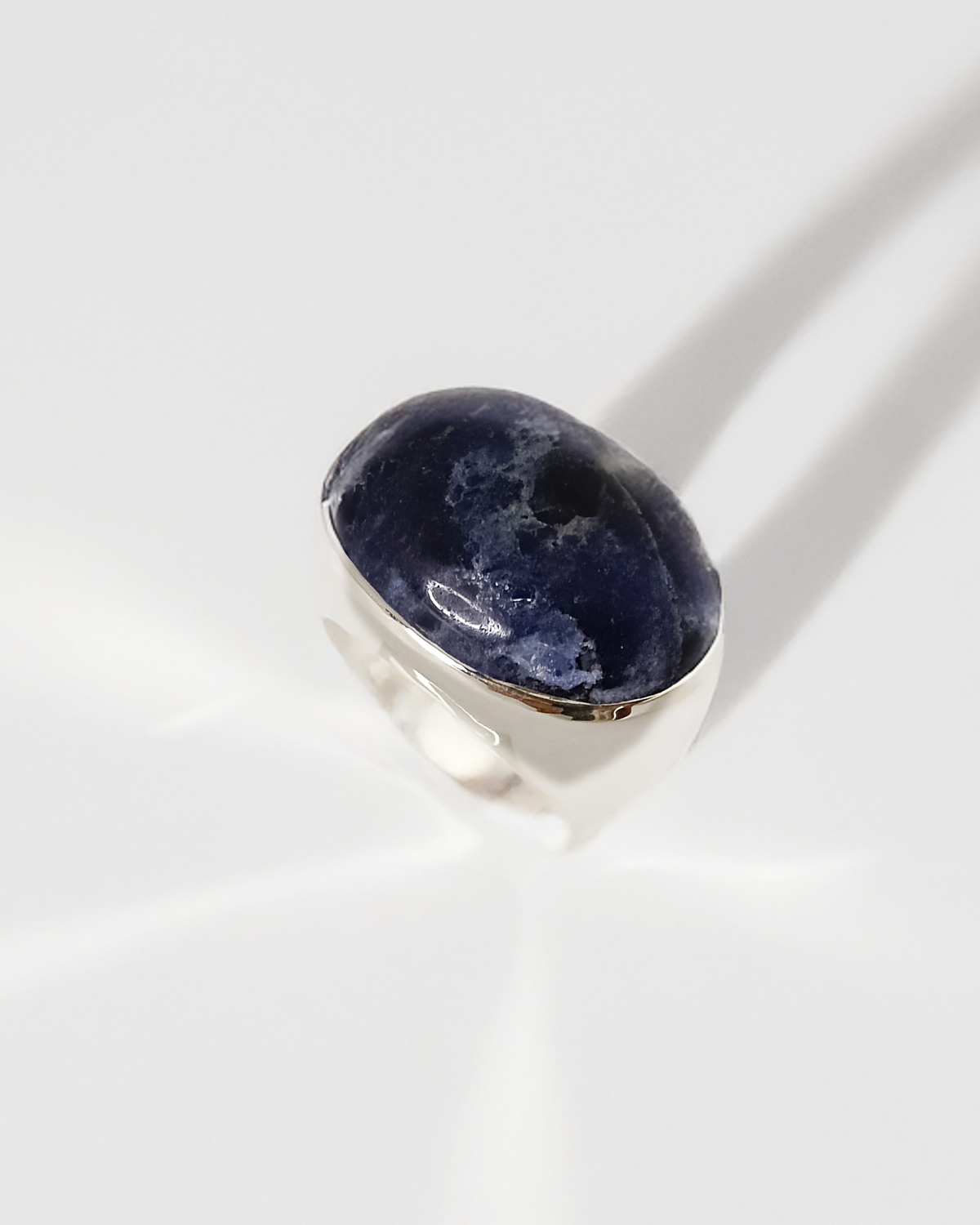 Silver ring with a dark blue gemstone on a white background. Natalie Noor, jewelry lit by desire.