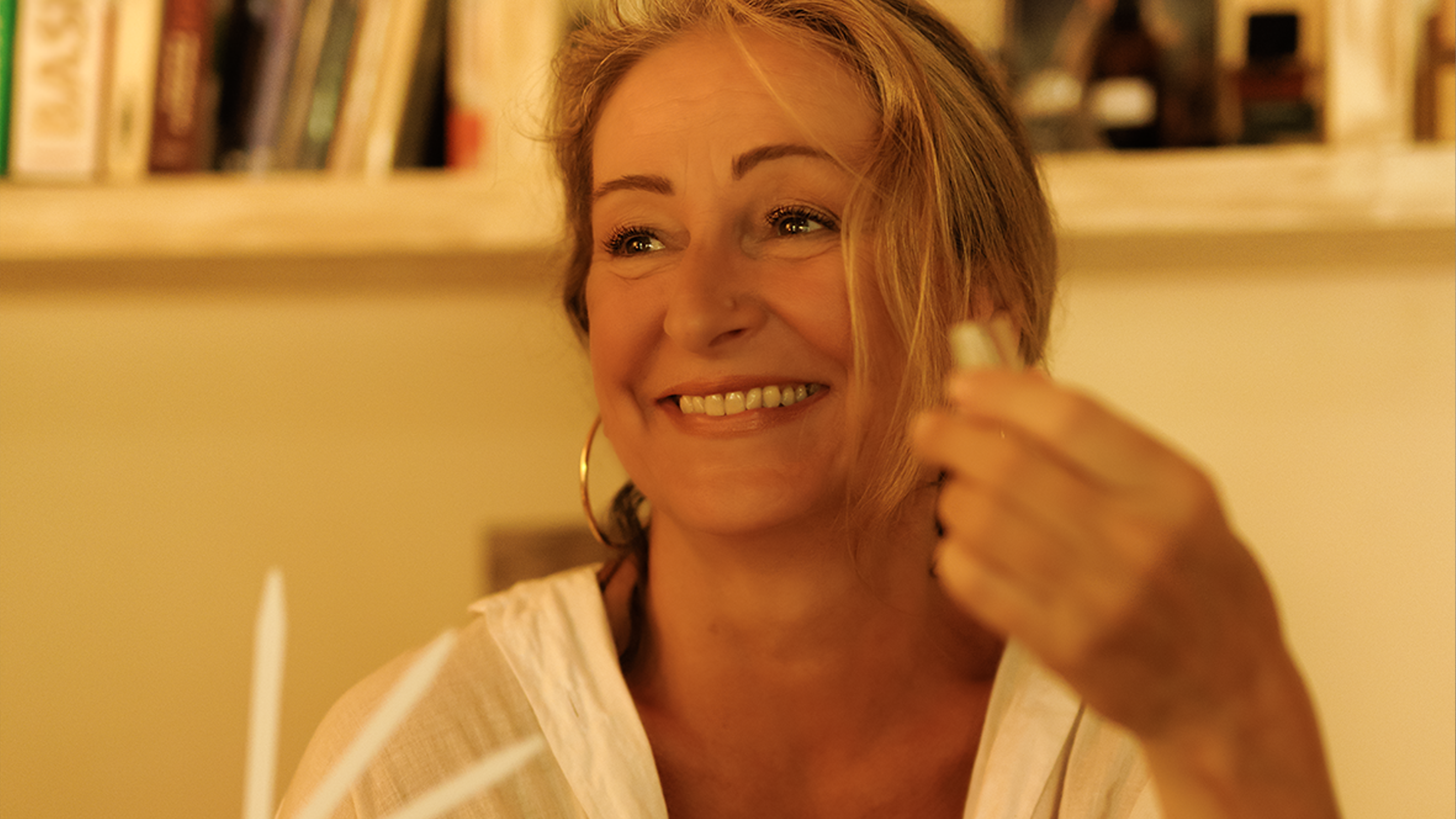Woman holding a small bottle of perfume close to her face in a blurred indoor setting. Natalie Noor.