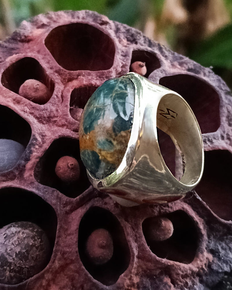 Silver ring with a green and golden apatite gemstone on a textured pink surface. Maison Natalie Noor, jewelry lit by desire.