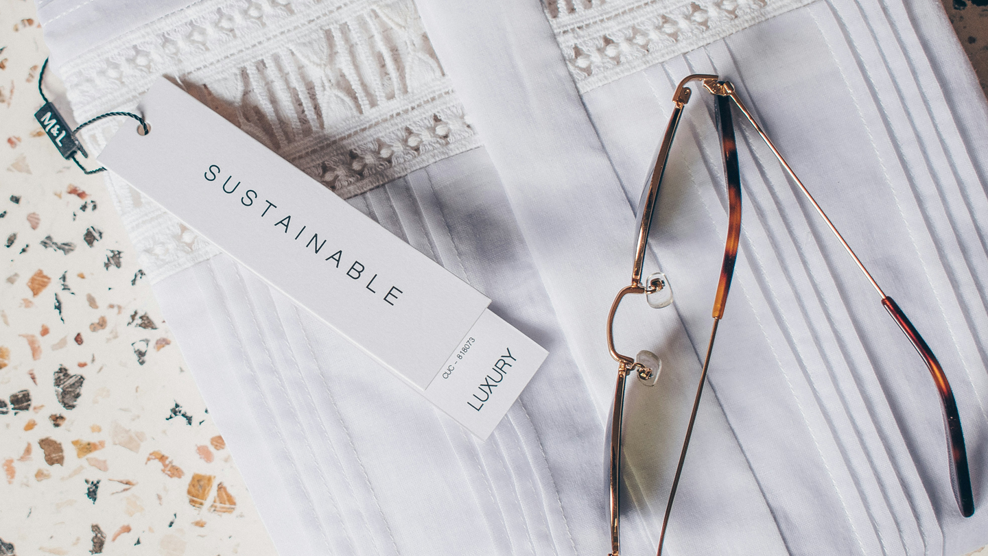 Eyeglasses with a 'Sustainable' label on a textured surface. 
