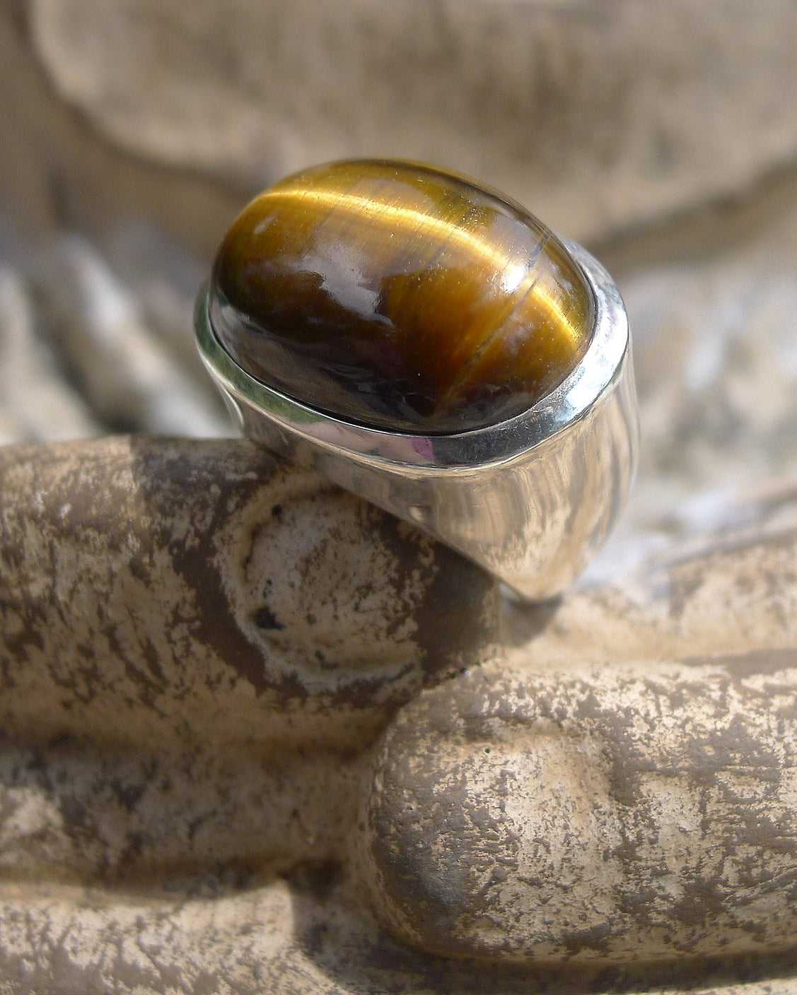 Silver ring with a tiger's eye gemstone on a textured surface. Maison Natalie Noor, jewelry lit by desire.