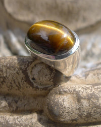 Silver ring with a tiger's eye gemstone on a textured surface. Maison Natalie Noor, jewelry lit by desire.