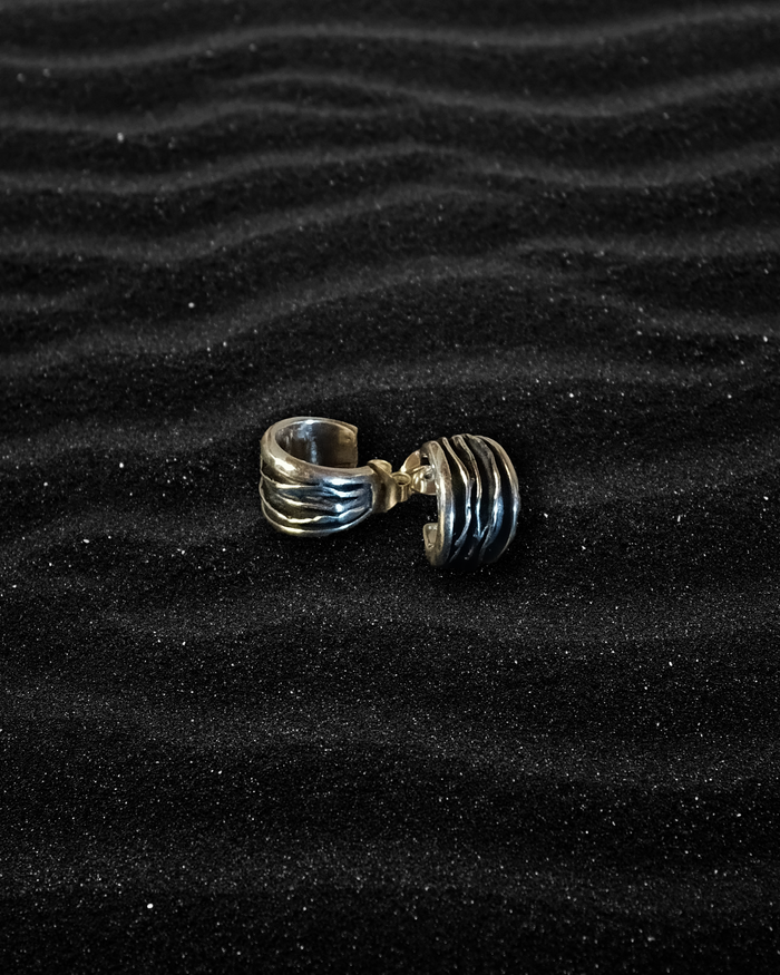 Silver earring with weavy patterns on a black sand background. Plisse technique. Maison Natalie Noor, jewelry lit by desire.