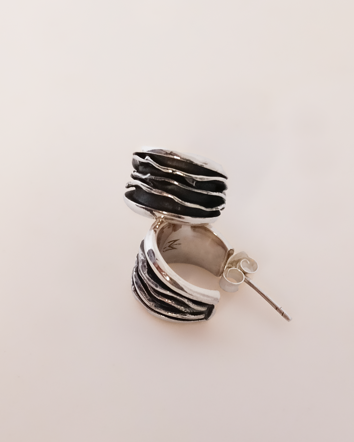 Silver and black layered earring on a light beige background. Plisse technique. Maison Natalie Noor, jewelry lit by desire.