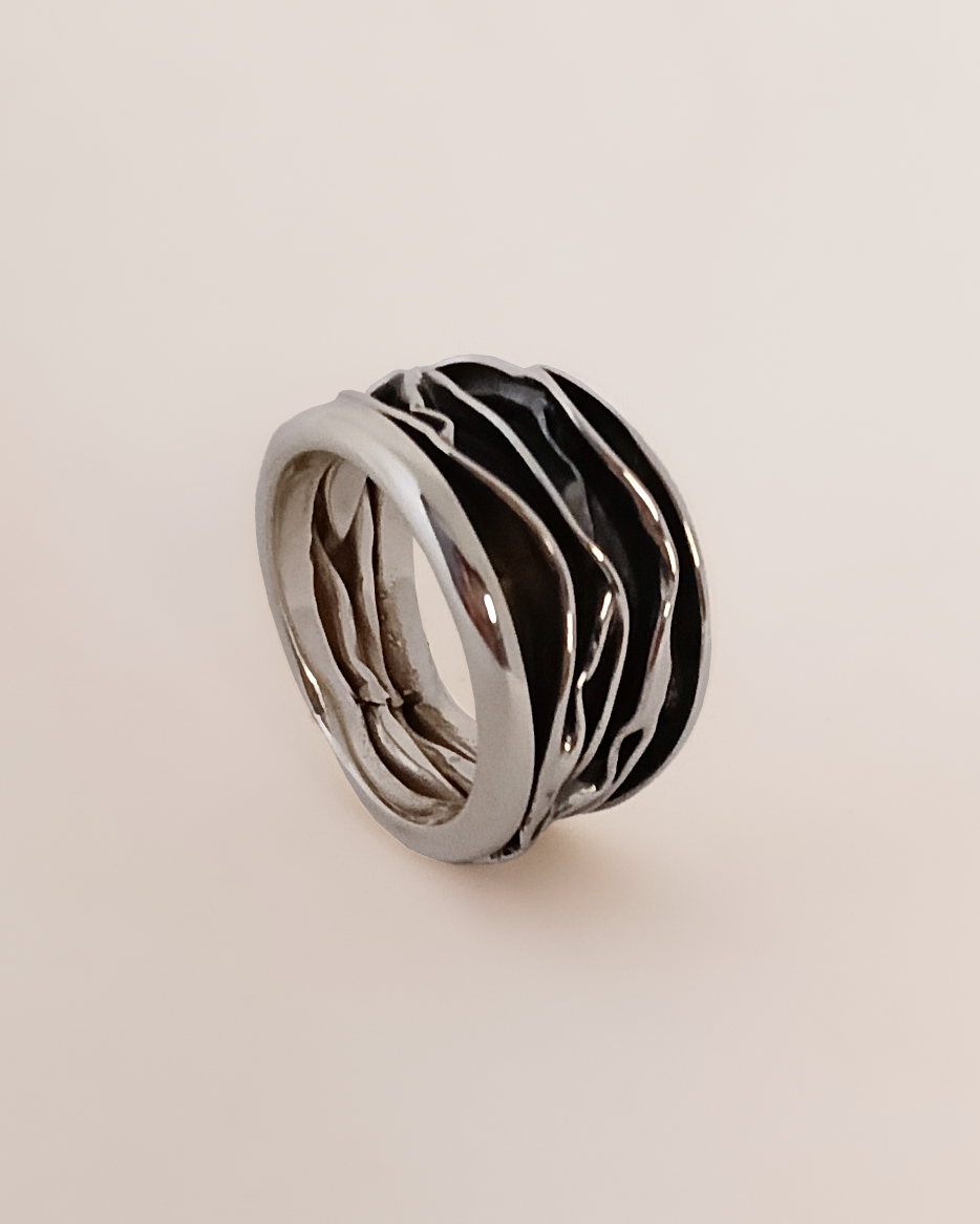 Silver ring with black pattern on a beige background. Maison Natalie Noor, jewelry lit by desire.