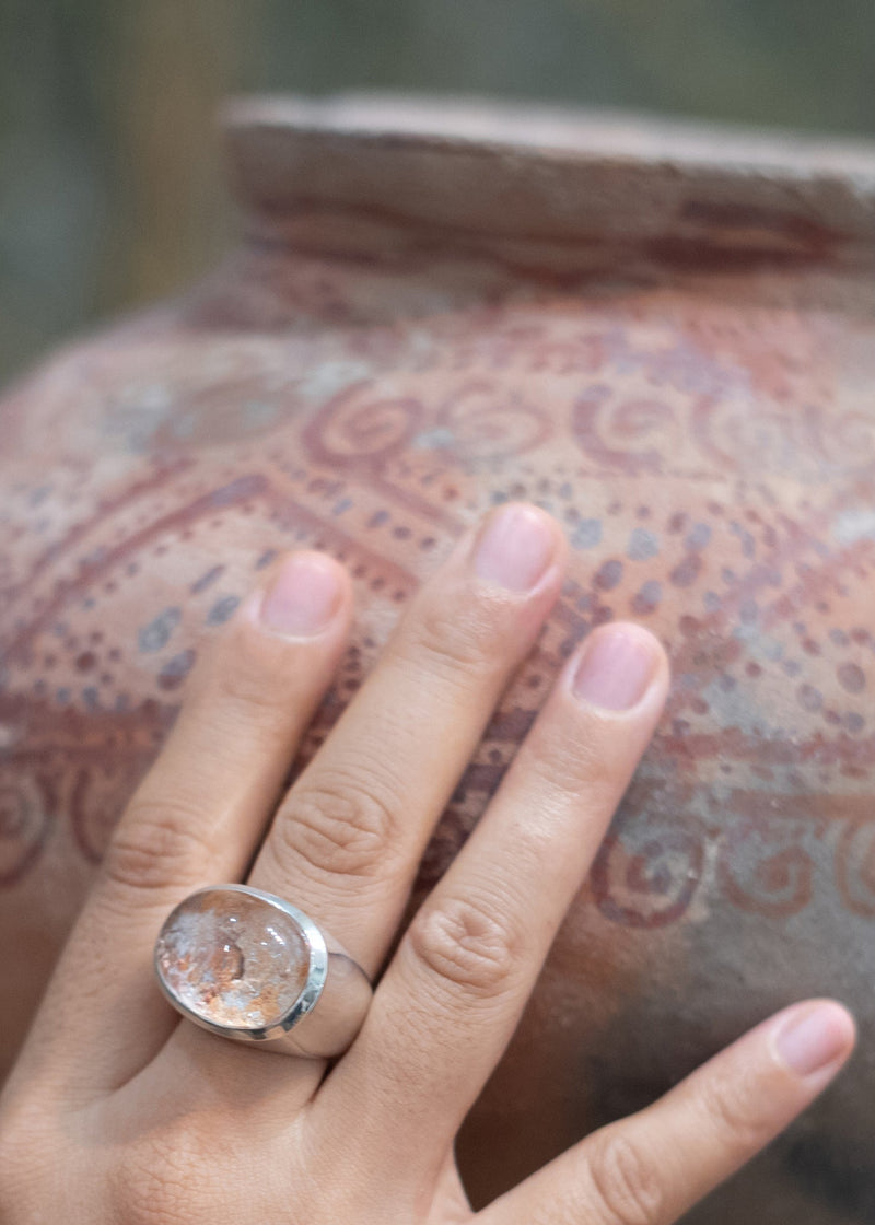 Hand with a ring holding a patterned vase, a lodolite, garden quartz gemstone cabochon signet ring on the middle-finger. Maison Natalie Noor, jewelry lit by desire.
