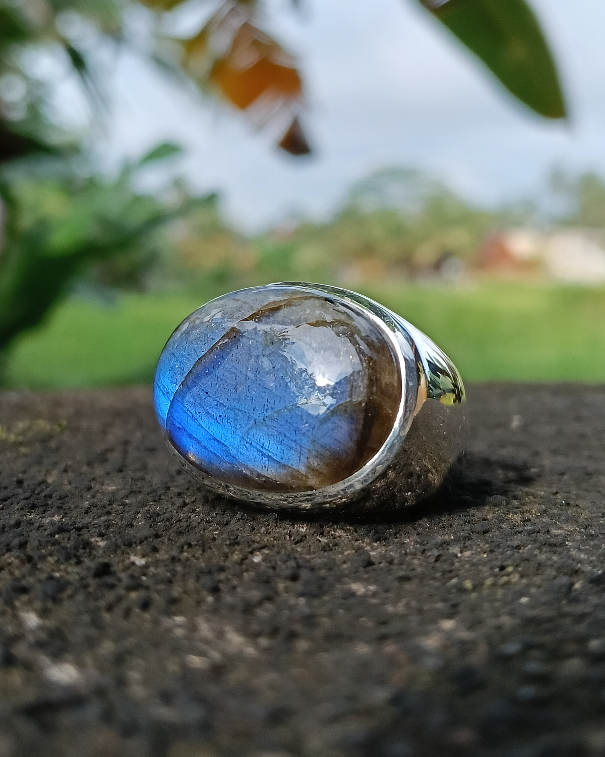 Silver ring with a blue labradorite gemstone on a textured surface with a blurred natural background. Maison Natalie Noor, jewelry lit by desire.