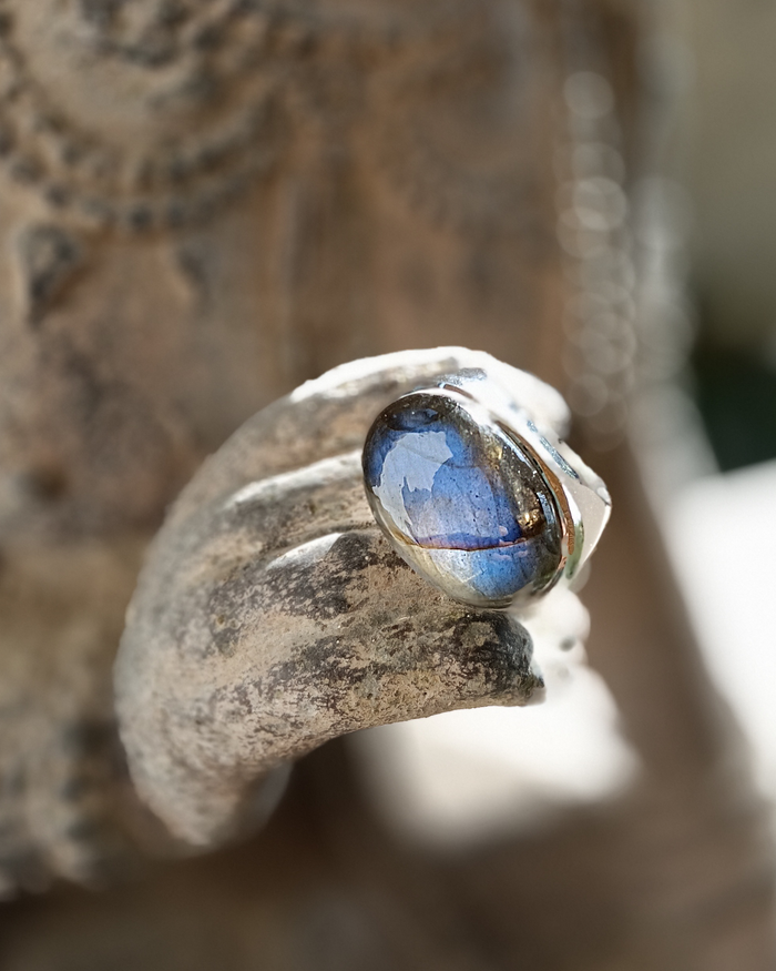Silver ring with a blue labradorite gemstone on a textured surface. Maison Natalie Noor, jewelry lit by desire.