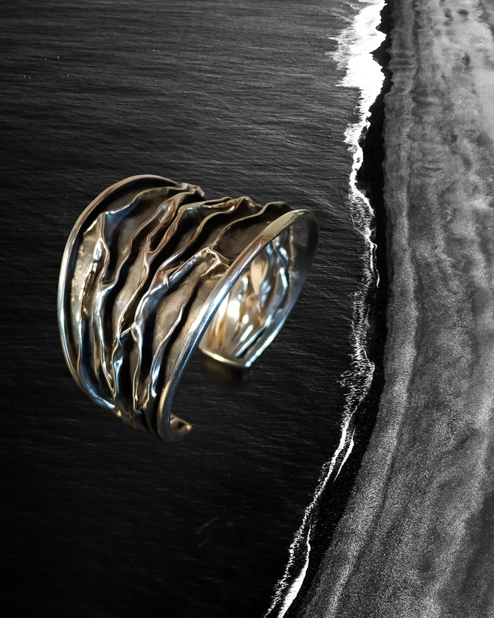Silver Cuff bracelet with wavy design on a black and white beach background. Maison Natalie Noor, jewelry lit by desire.