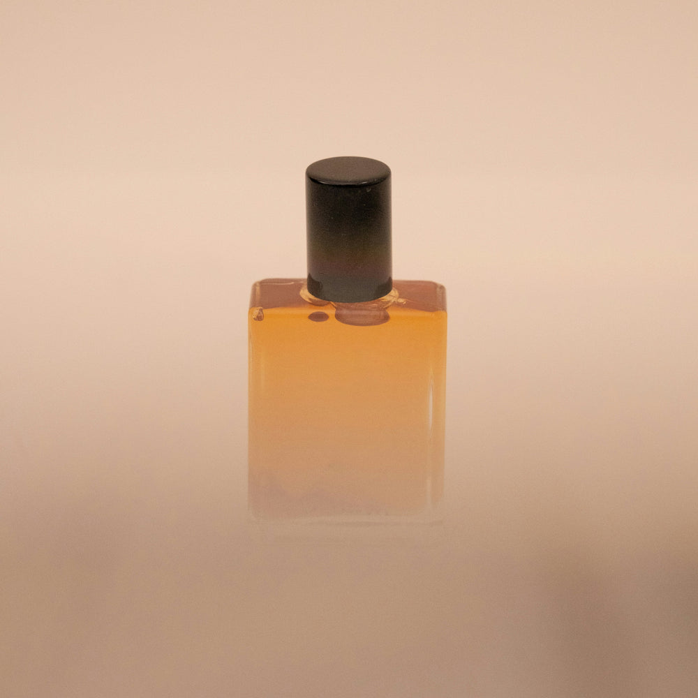 Amber-colored bottle with a black cap on a beige background. Fragrant Portal by Natalie Noor