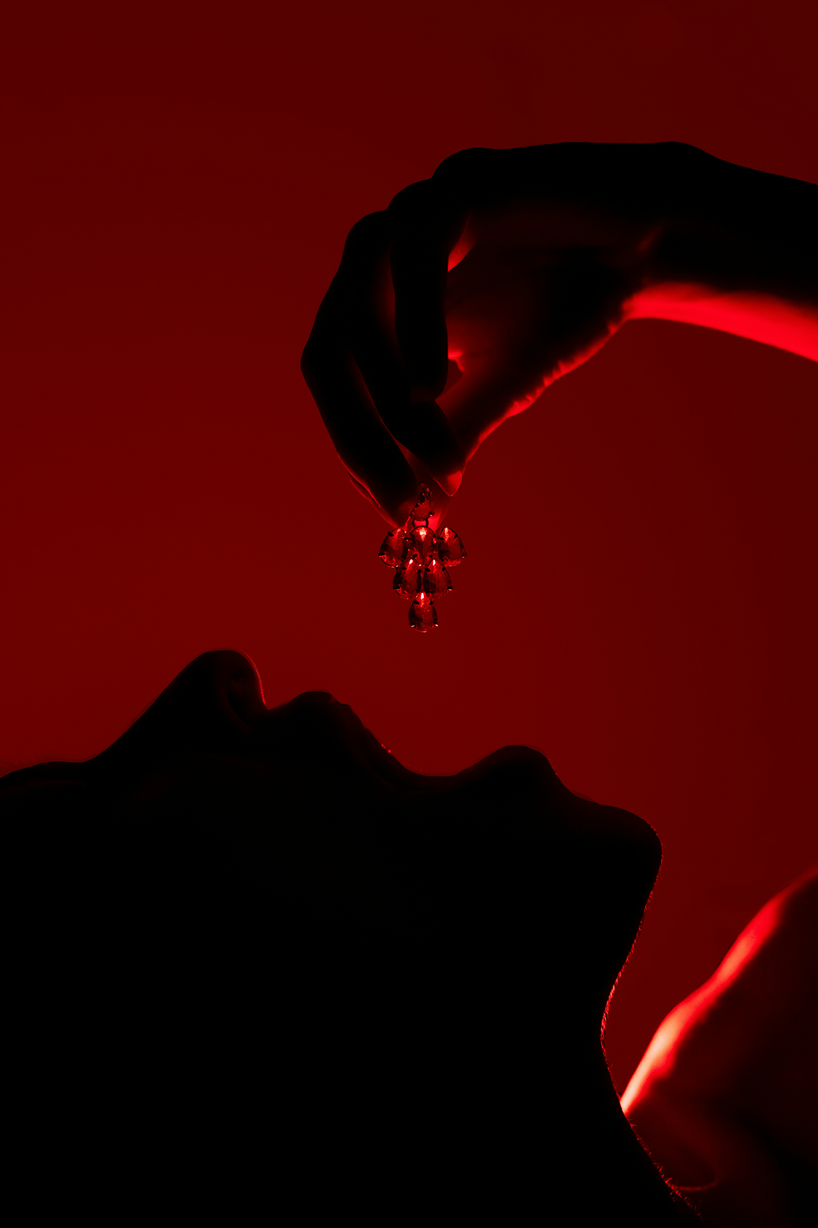 Silhouette of a hand holding a small object against a red background Jewelry lit by desire - Natalie Noor