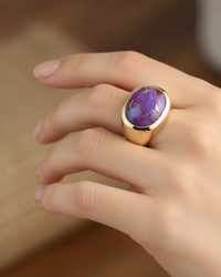 Hand wearing a gold ring with a purple stone on a blurred background