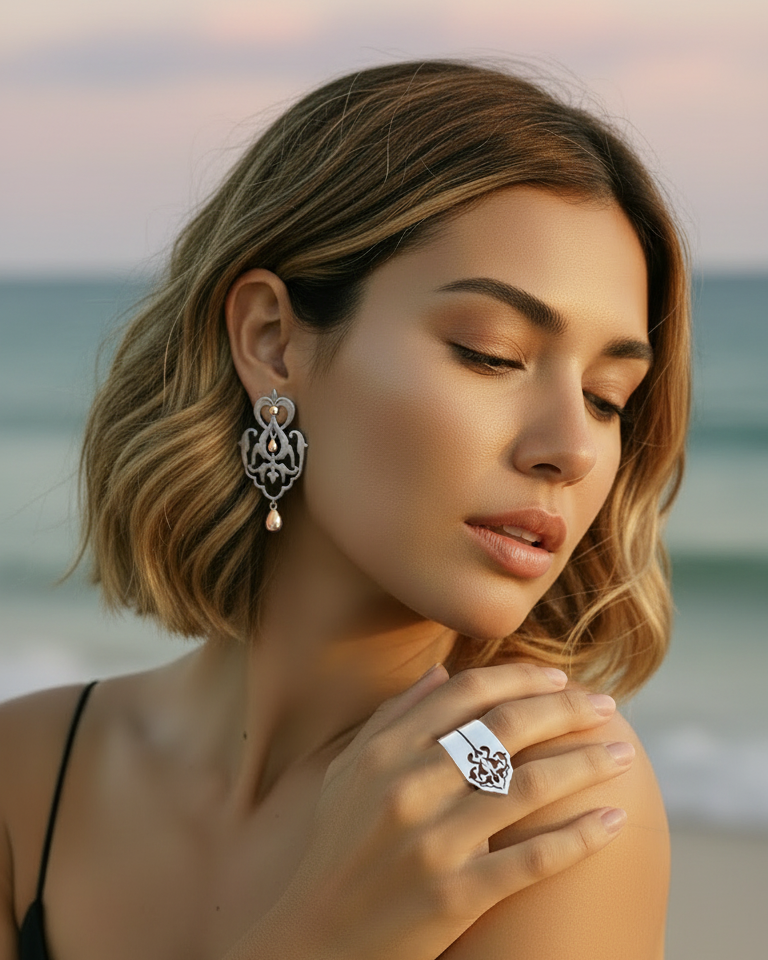 Woman on a beach wearing earrings and a ring with a scenic background. Sharafeh collection, jewelry lit by desire, maison natalie noor