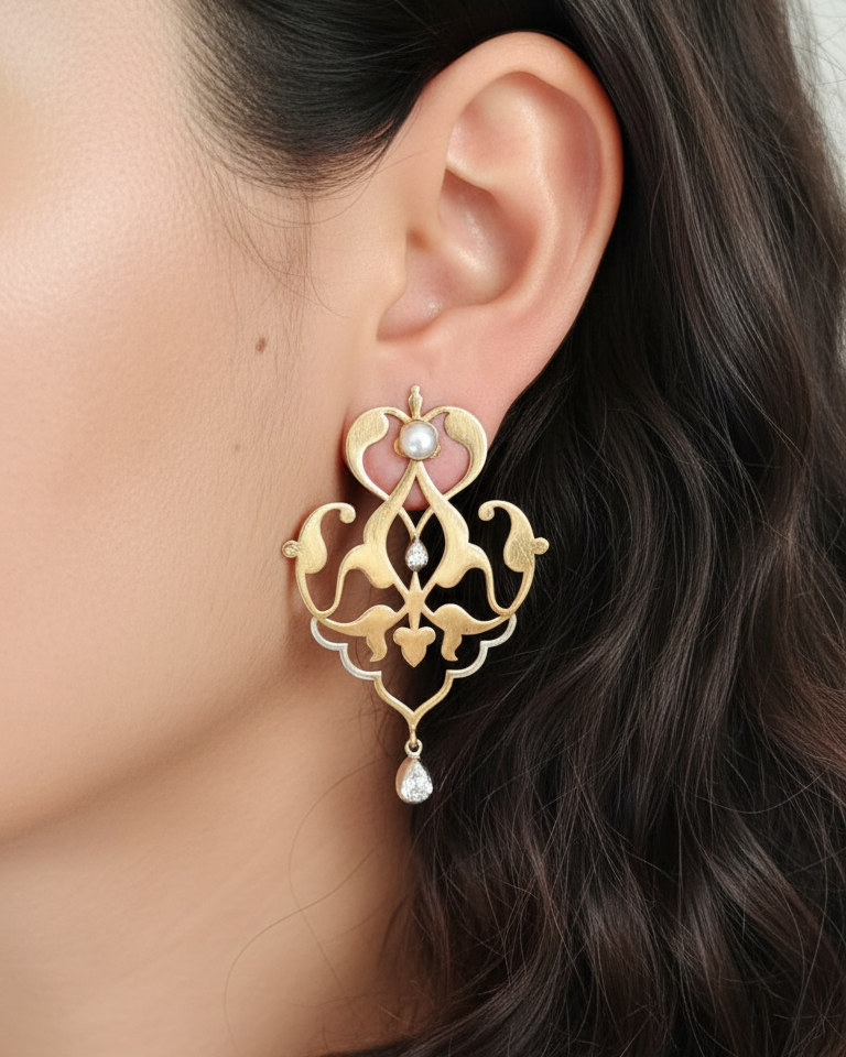 Gold earrings worn by a woman with dark hair. Fine and stylish Gold and silver pearl earrings on a beige background. Maison Natalie Noor, Sharafeh Collection - Jewelry lit by Desire