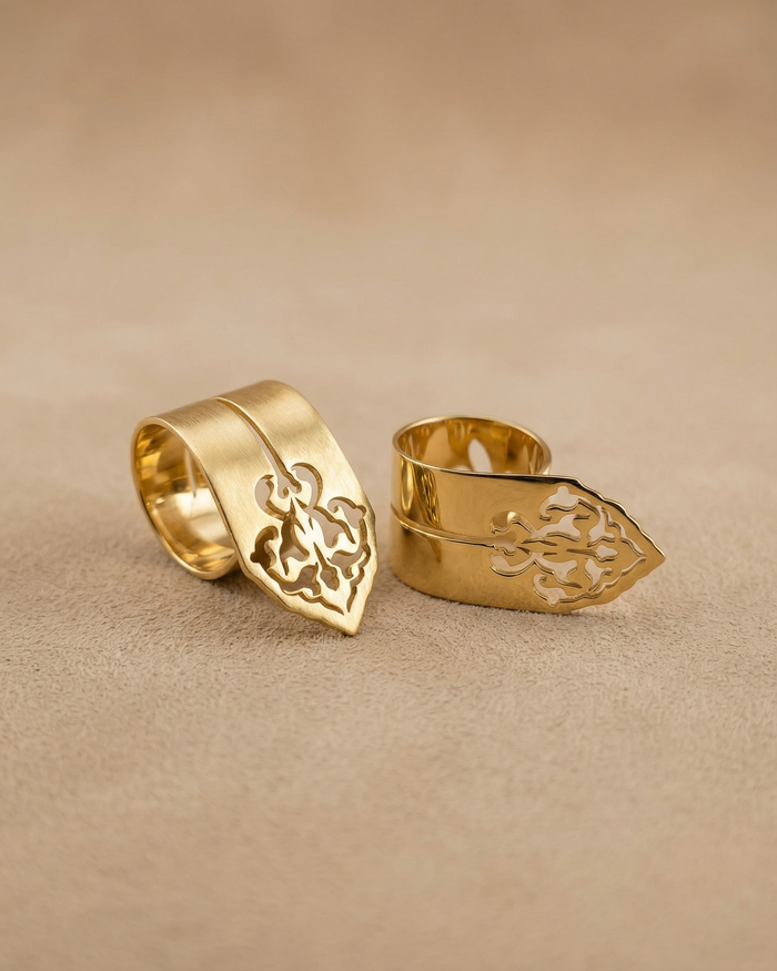 Two gold rings with intricate designs on a beige background from the Sharafeh Collection, jewelry lit by desire by Natalie Noor.